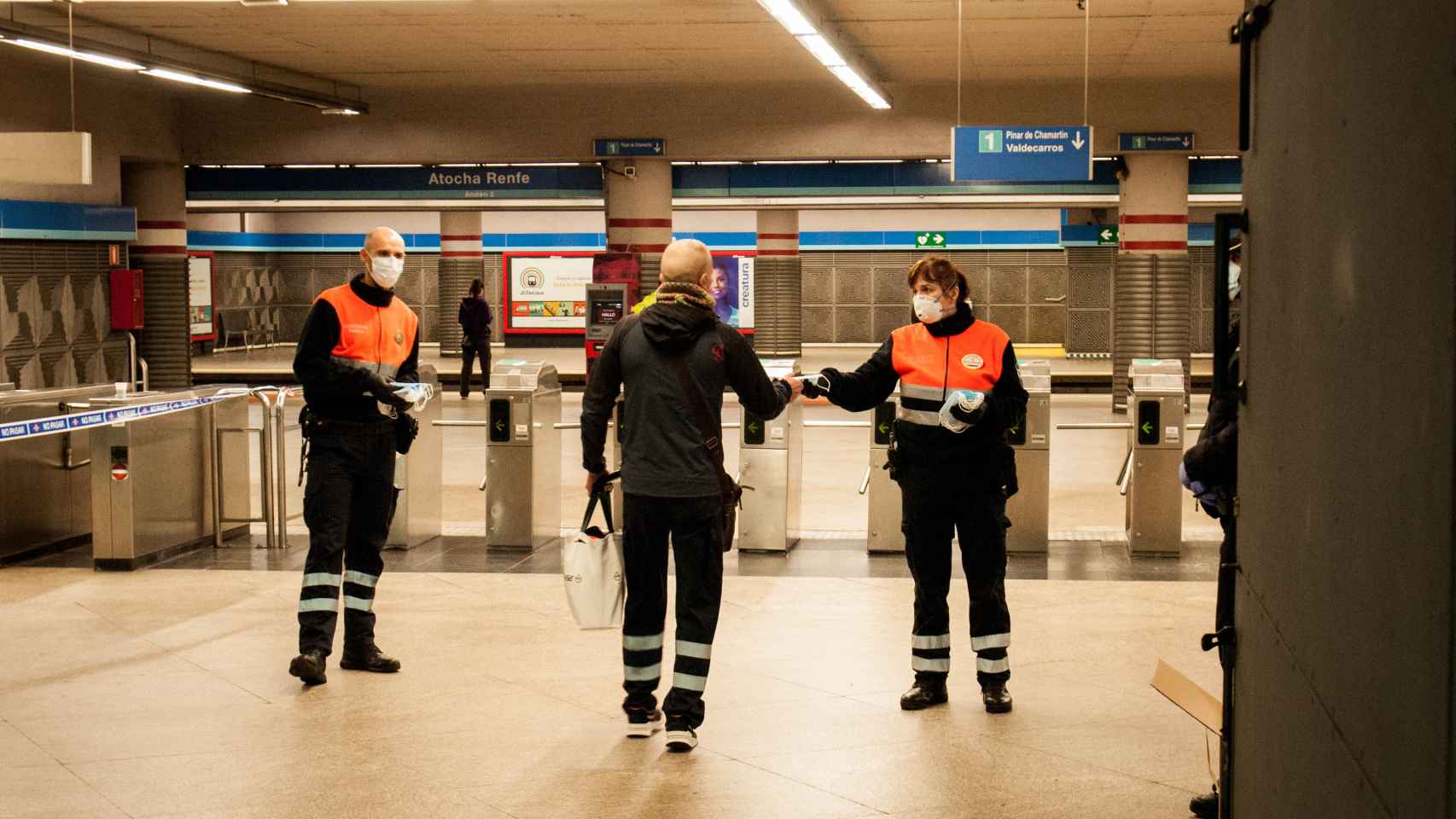 El personal de seguridad reparte mascarillas a la entrada de la estación de Atocha Renfe.