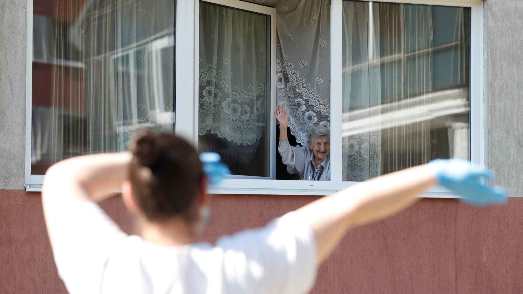 Una anciana se asoma a la ventana de la residencia en la que vive para disfrutar de la música que suena en la calle.
