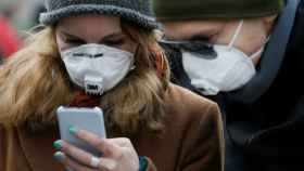 FILE PHOTO: People wearing protective face masks use a smartphone on a street in Kiev