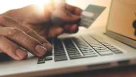 Una persona usando un ordenador con tarjeta de crédito y haciendo compras online.