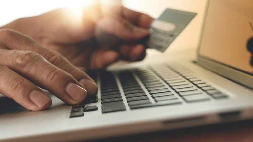 Una persona usando un ordenador con tarjeta de crédito y haciendo compras online.