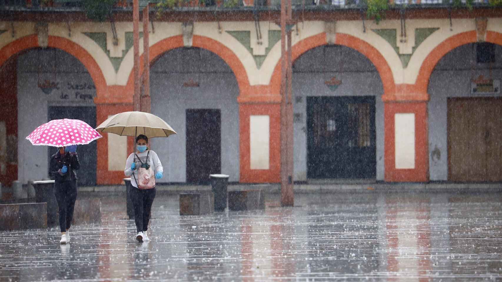 Dos mujeres protegidas con mascarillas y paraguas caminan por Córdoba. EFE/Salas