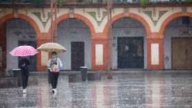 Dos mujeres protegidas con mascarillas y paraguas caminan por Córdoba. EFE/Salas
