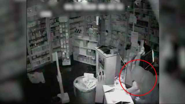 Uno de los ladrones, asaltando la caja registradora de una farmacia.