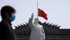 Una mujer con mascarilla pasa delante de una estatua de  Mao Zedong en Wuhan.