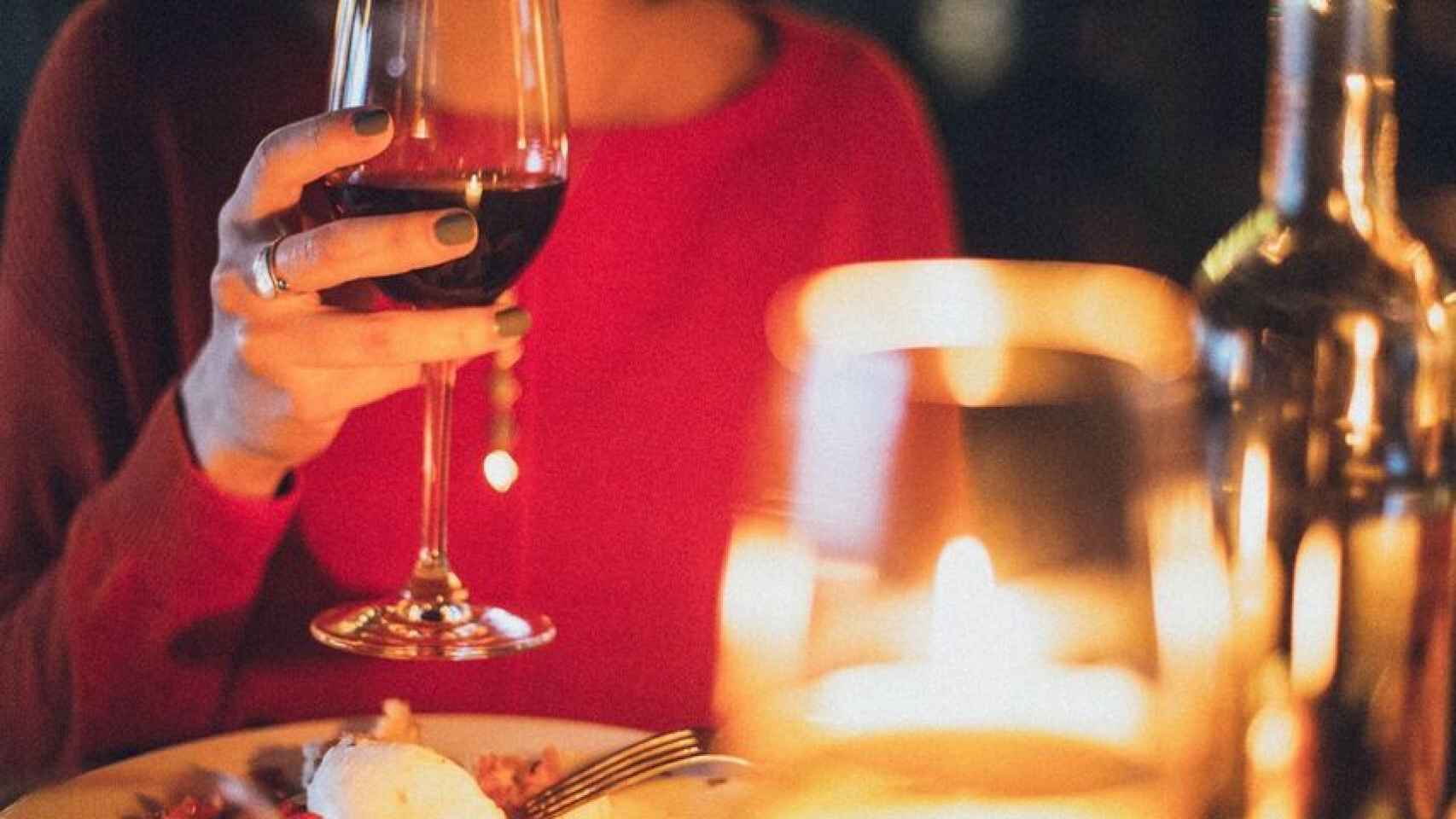 Una mujer cena con un vino tinto.