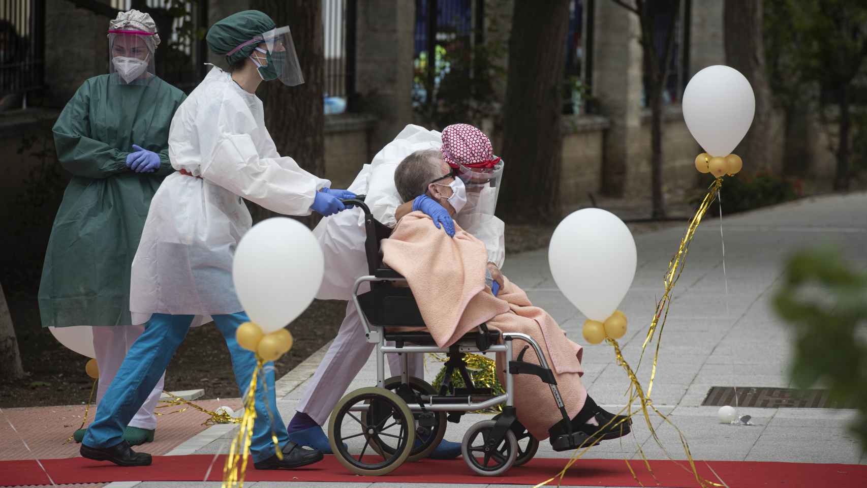 Una anciana en silla de ruedas recibe el cariño del personal sanitario en una residencia.