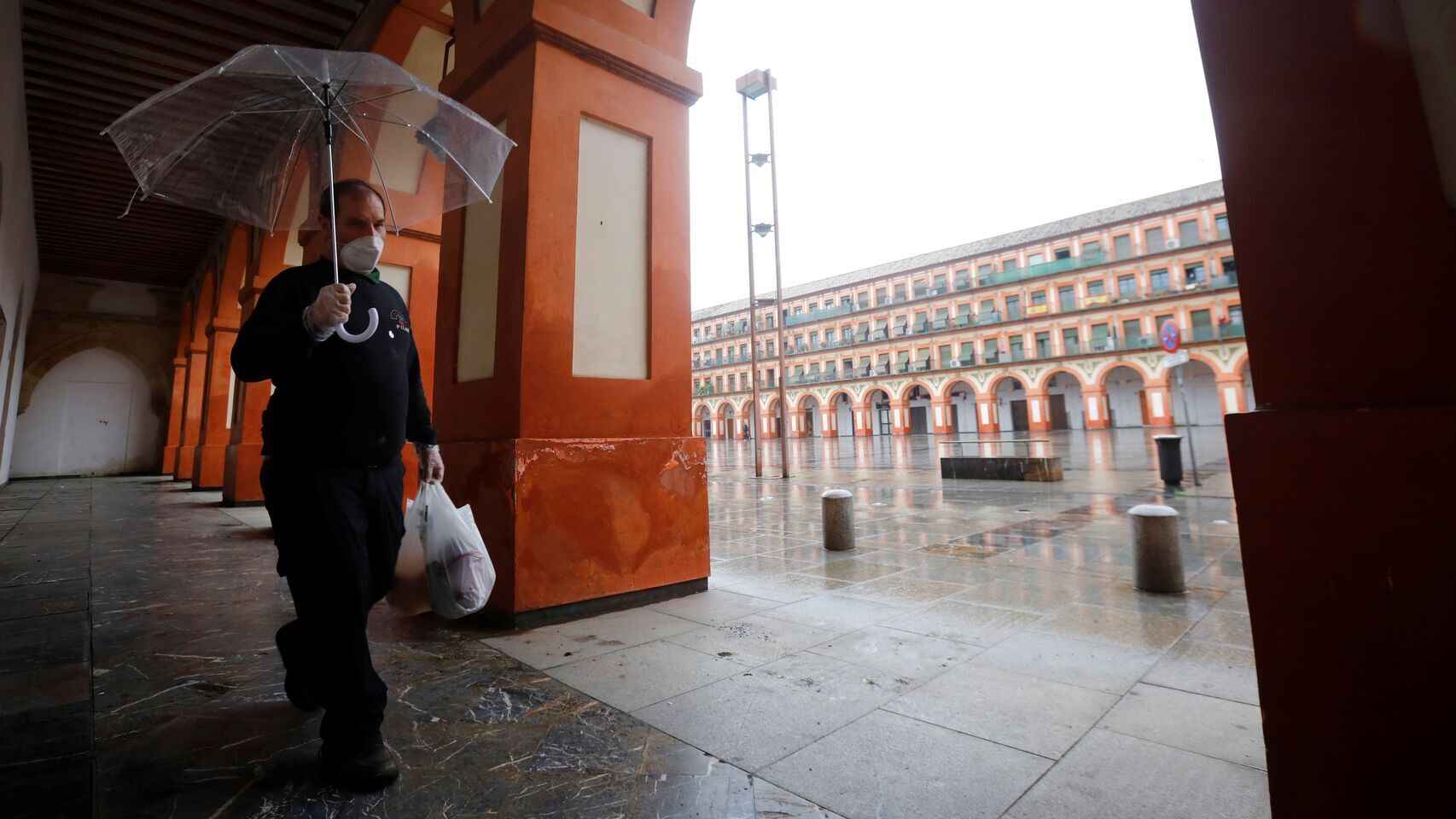 Un hombre protegido con mascarilla y paraguas camina este lunes por la Plaza de la Corredera de Córdoba.