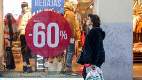 Una mujer pasea junto a una tienda de moda de Madrid, en la que se ofertan las segundas rebajas.