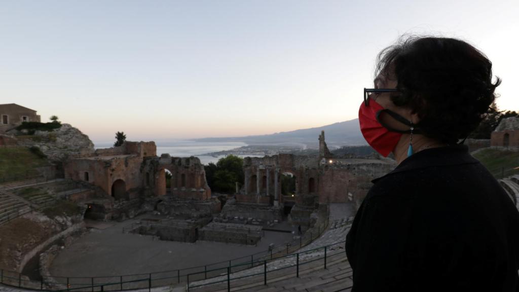 Una mujer con una mascarilla protectora se encuentra en el teatro greco-romano de Taormina, Sicilia.