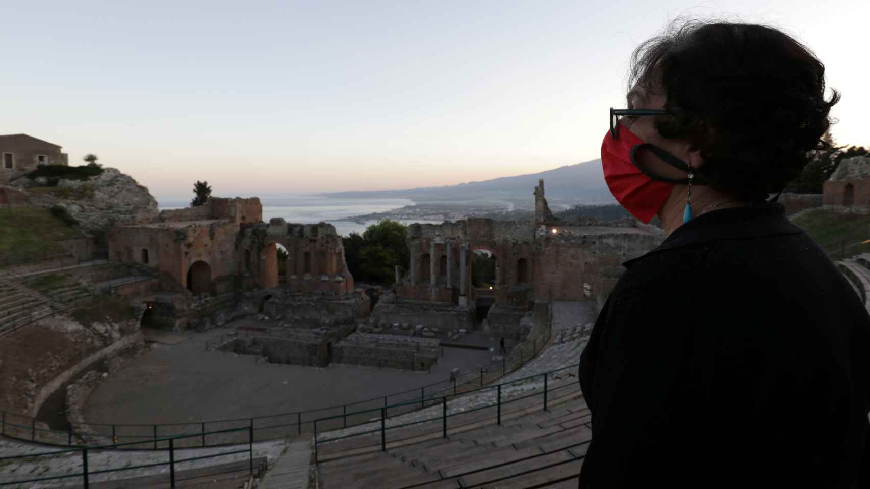 Una mujer con una mascarilla protectora se encuentra en el teatro greco-romano de Taormina, Sicilia.