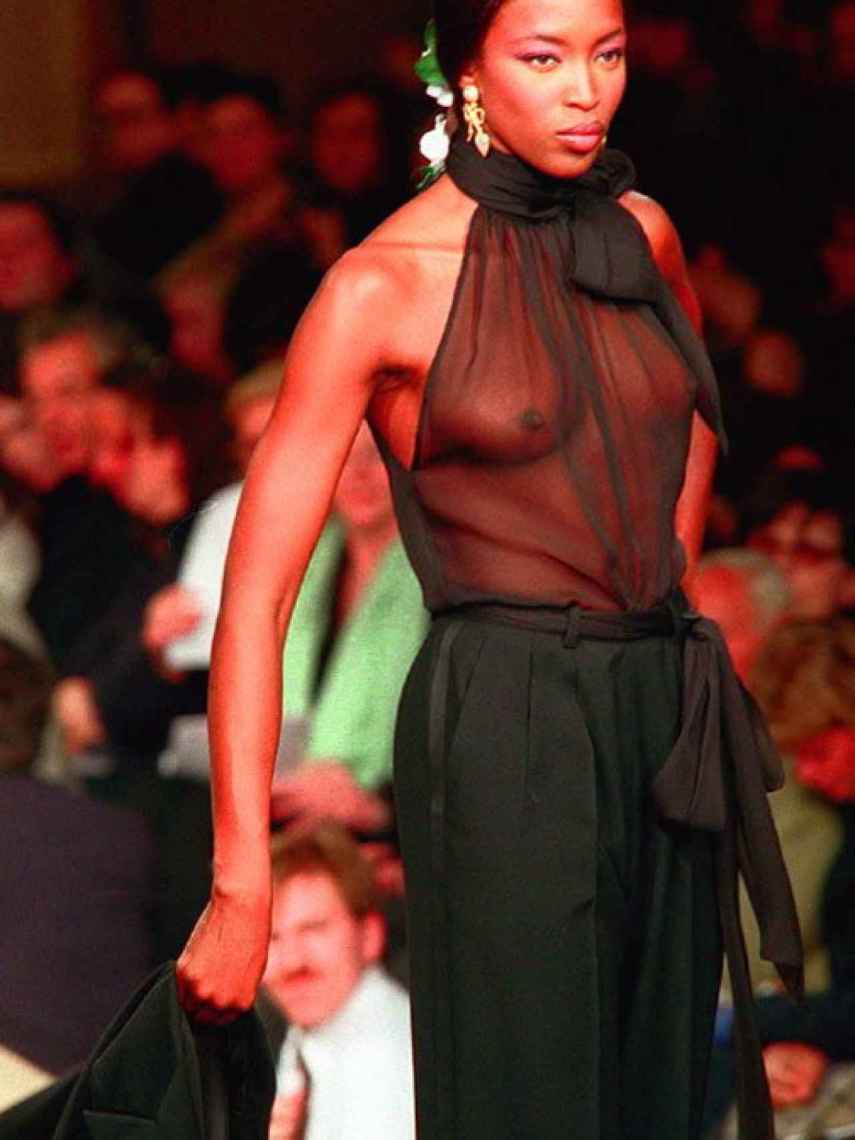 Naomi Campbell con una bluse negra trasnparente desfilando para Yves Saint Laurente en la primavera/verano de 1999.