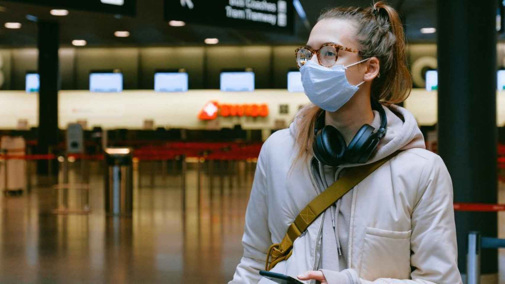 Una joven, llevando gafas y mascarillas en un aeropuerto.