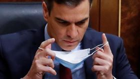 Pedro Sánchez en su escaño del Congreso colocándose la mascarilla.