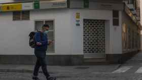 Un hombre protegido con mascarilla camina delante de una oficina de empleo.