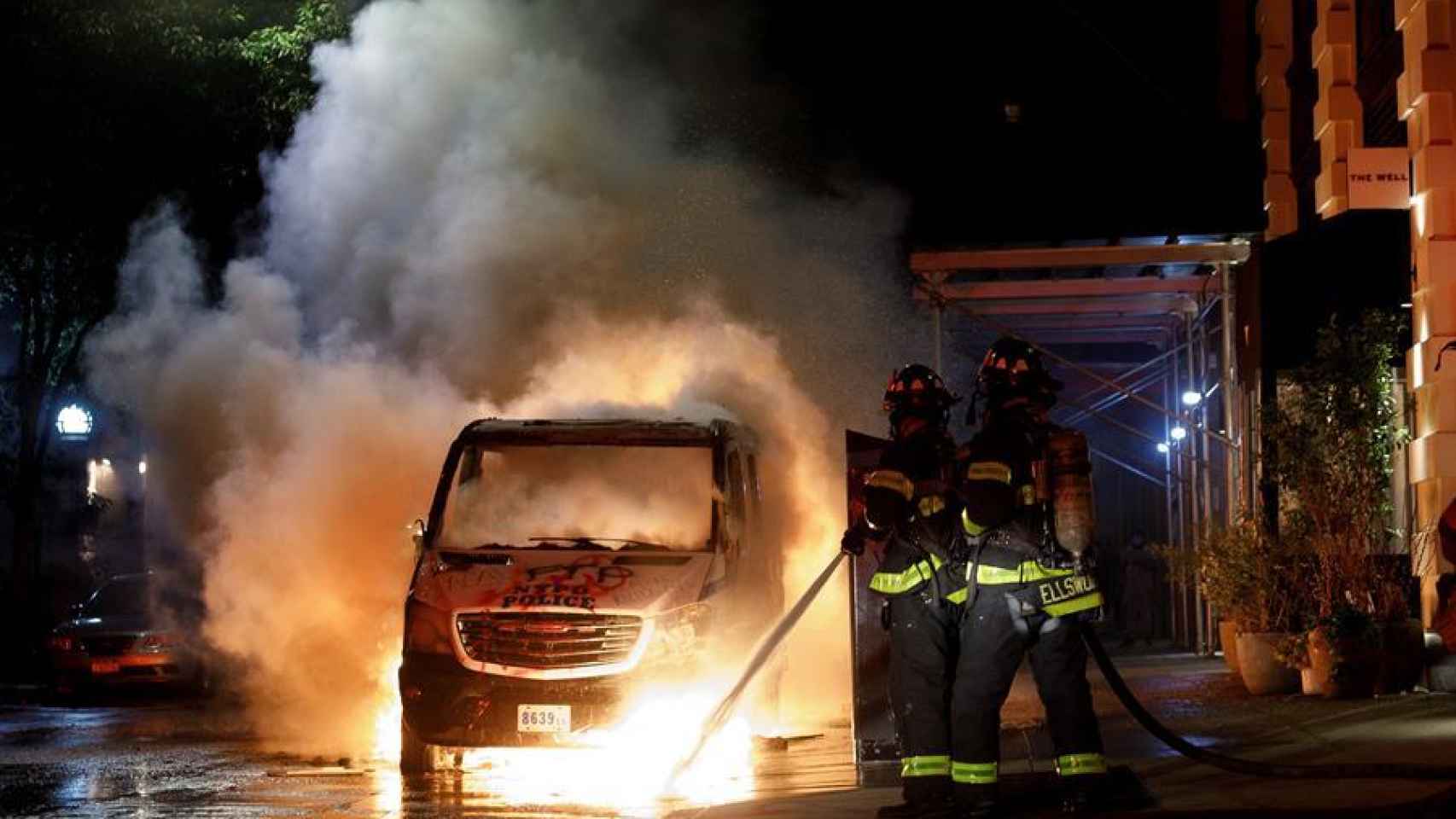 Los servicios de emergencias apaciguan un coche incendiado por los manifestantes.