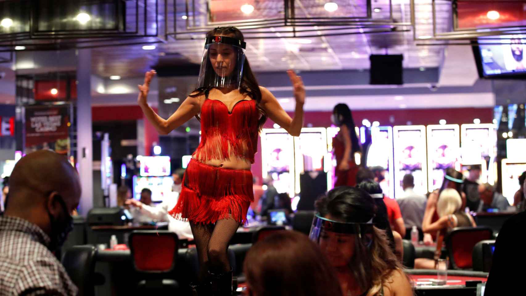 Una mujer baila detrás de una mesa de juego llevando una pantalla protectora.