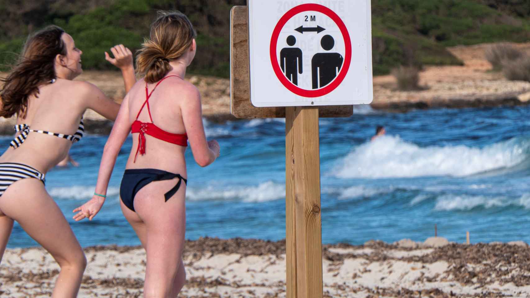Un cartel informa de la obligatoriedad de guardar la distancia social en la playa de Sa Coma en Mallorca.