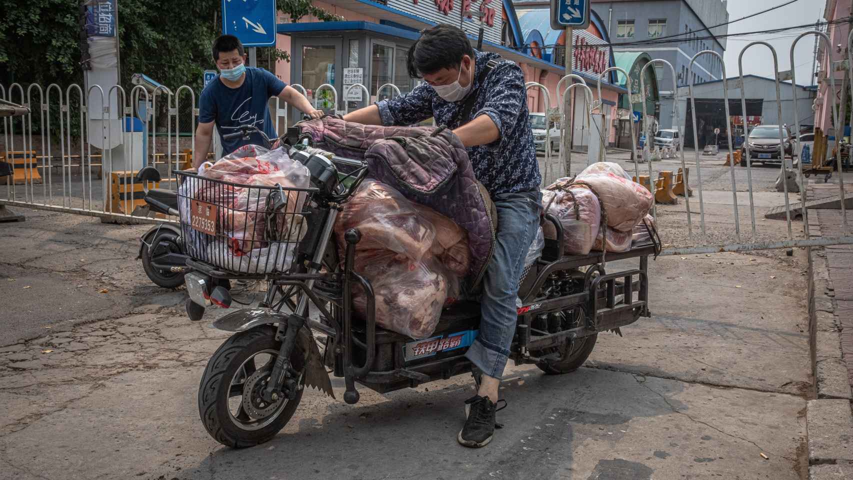 Hombres con máscaras protectoras cargan un scooter con carne al lado del edificio cerrado del mercado Xinfadi.