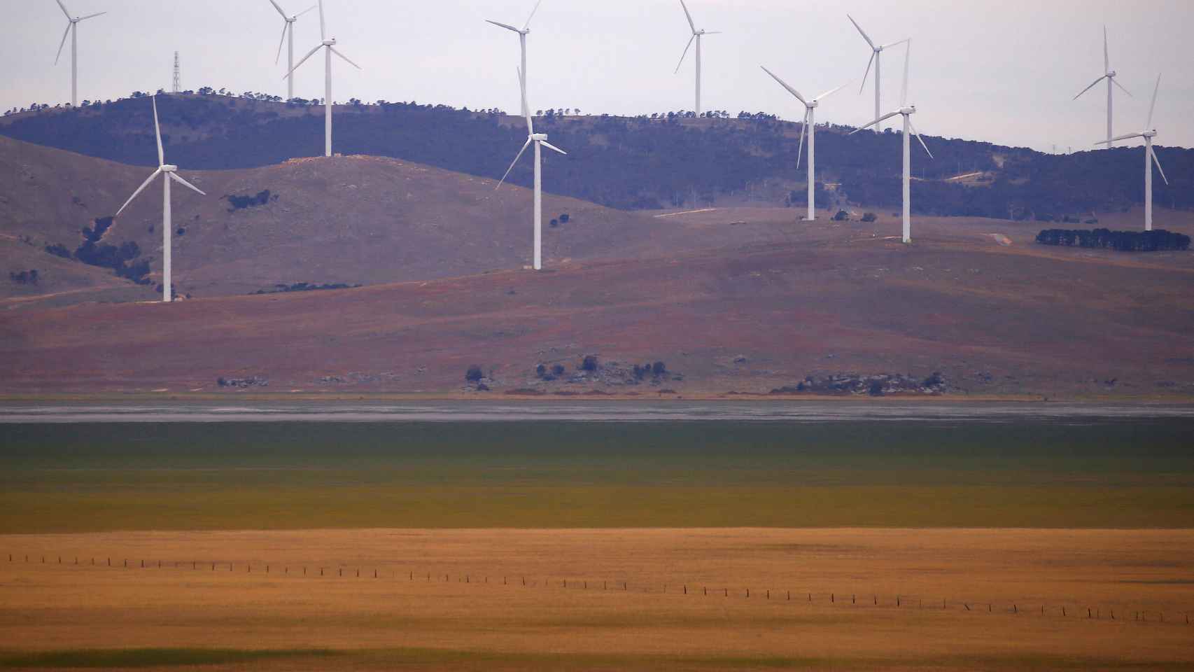 FILE PHOTO: A fence is seen in front of wind turbines that are part of the Infigen Energy Capital Wind Farm located on the hills surrounding Lake George, near the Australian capital city of Canberra
