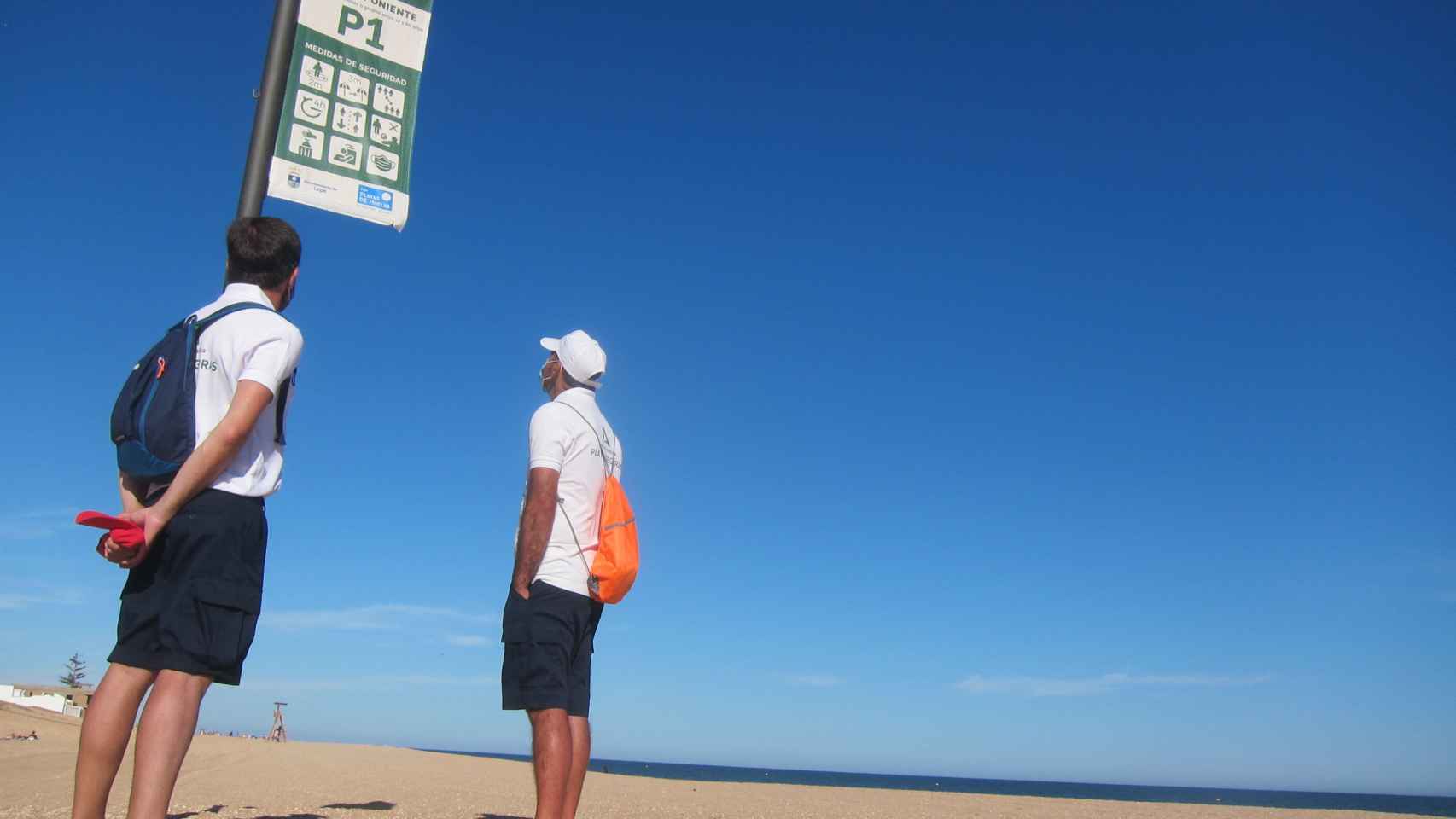 Los vigilantes de la playa junto a un cartel con las recomendaciones en La Antilla (Huelva).