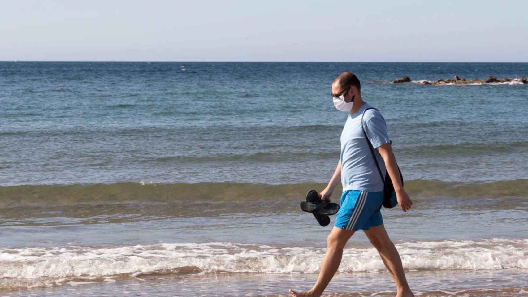 Una persona pasea por la playa con mascarilla. Efe