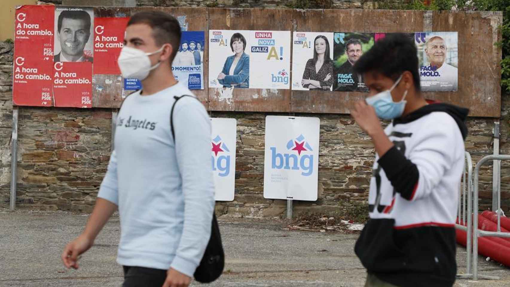 Dos jóvenes con mascarillas pasan por delante de varios carteles electorales, este viernes en Foz (Lugo).