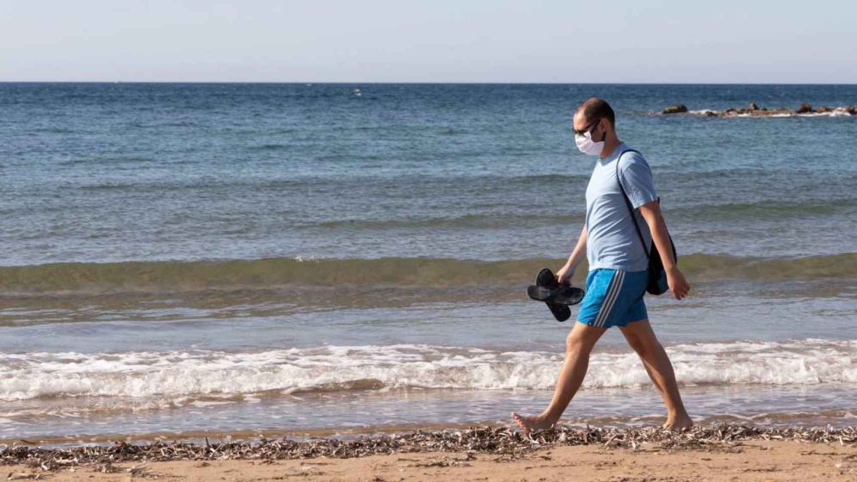 Un hombre con una mascarilla pasea por la playa