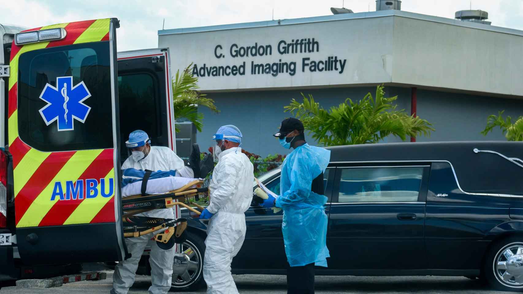 Trabajadores de emergencias del North Shore Medical Center de Miami trasladan a un paciente mientras pasa el coche de una funeraria.
