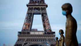 Varias estatuas con mascarilla delante de la Torre Eiffel.