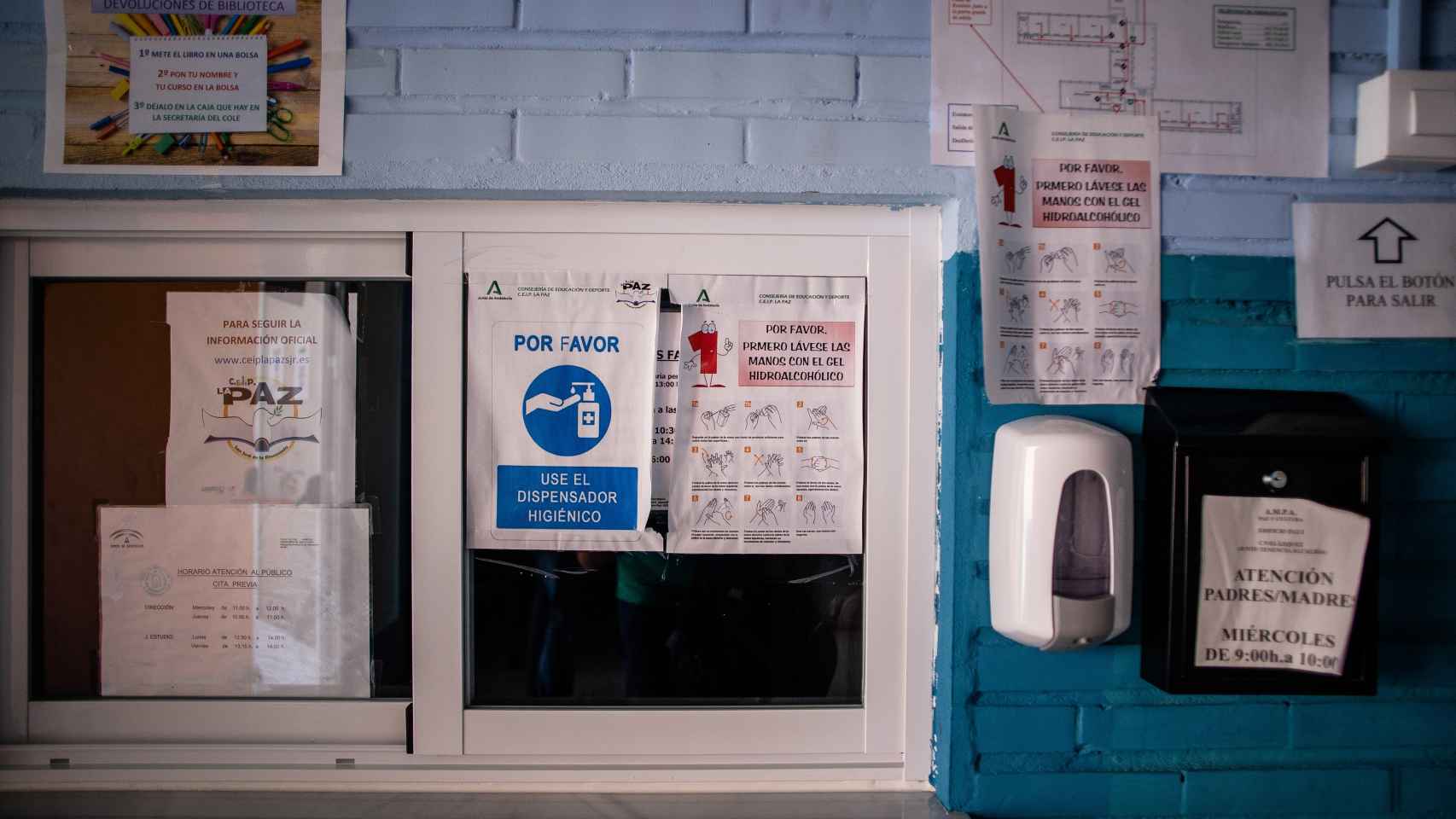 Un dispensador de gel hidroalcohólico junto a carteles informativos en la ventanilla de secretaría.