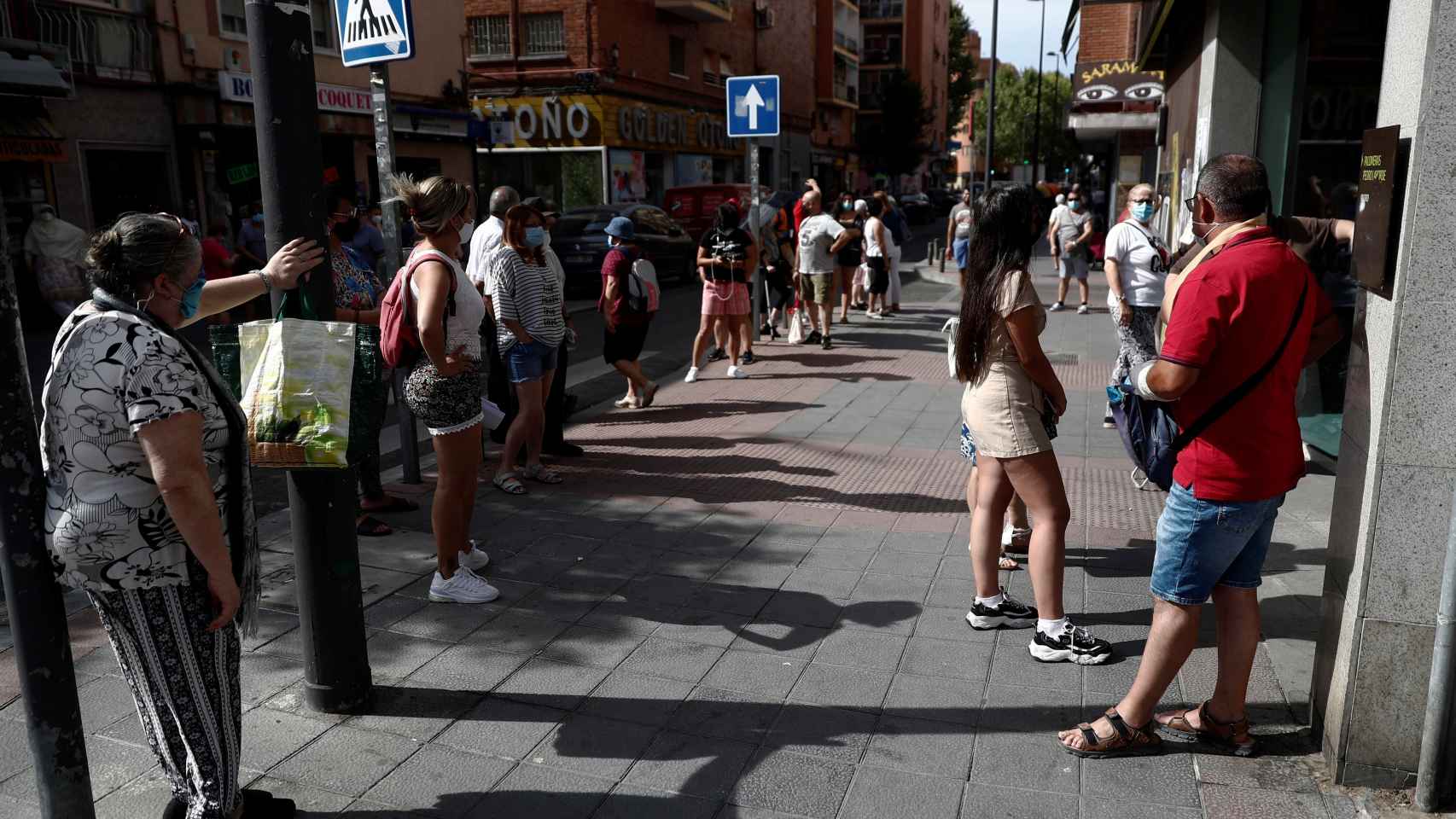 Unas personas pasan calor haciendo cola para entrar al banco en Madrid.