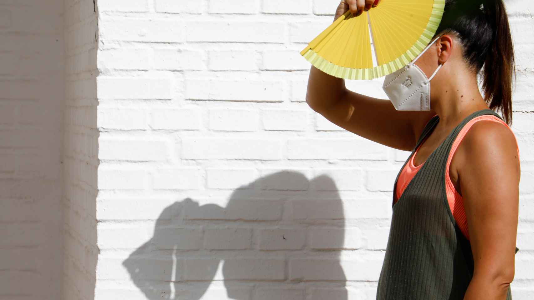 Una mujer con mascarilla se protege del sol con un abanico en Córdoba.