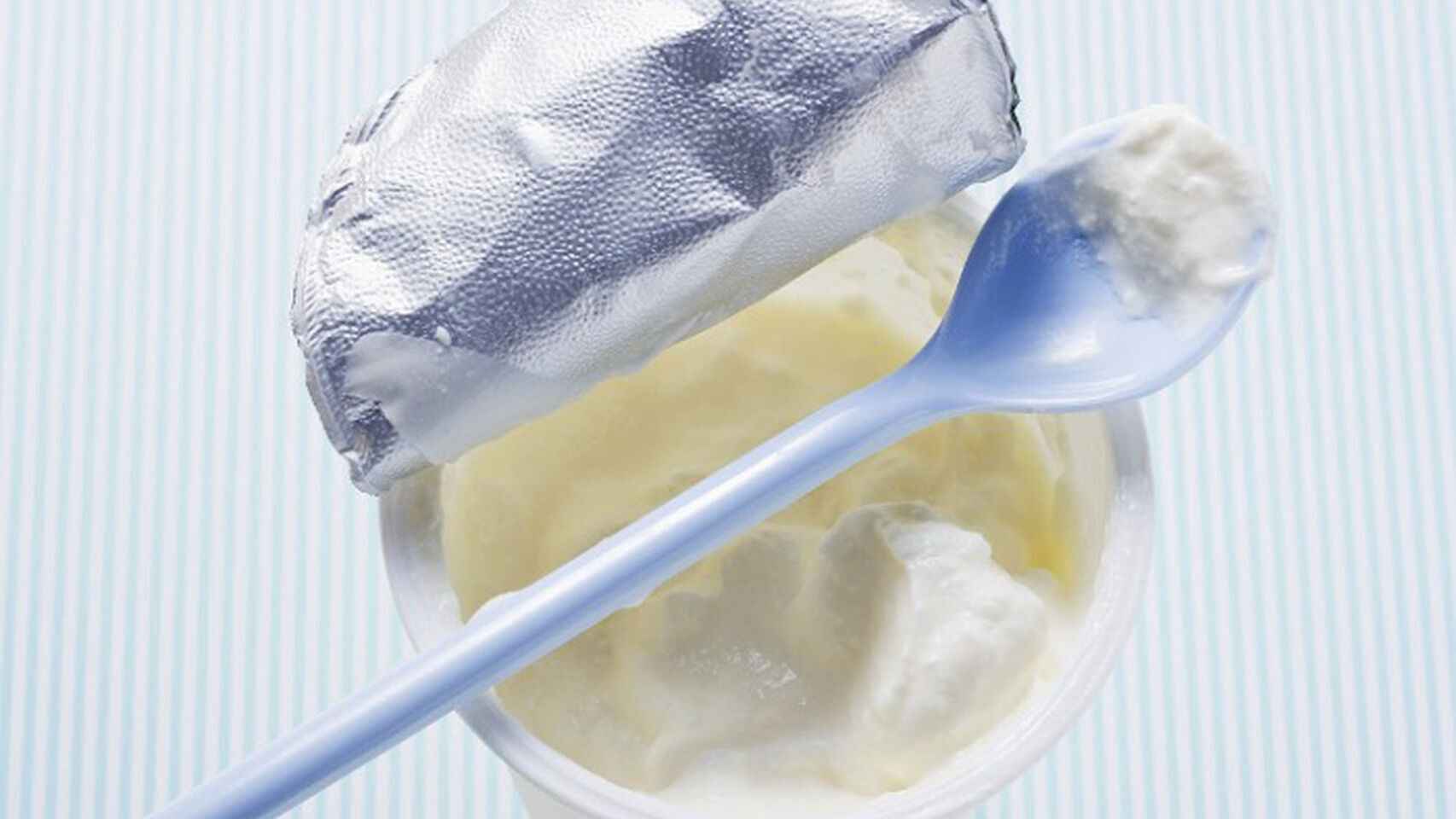 Un yogur griego abierto con una cucharilla sobre su superficie.