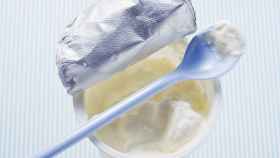 Un yogur griego abierto con una cucharilla sobre su superficie.