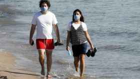 Un hombre y una mujer paseando en la playa con mascarilla.