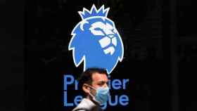 Un hombre con mascarilla frente al logo de la Premier League