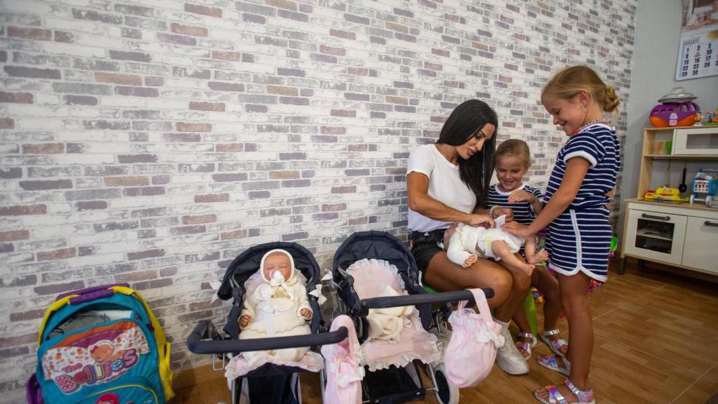 Las gemelas Elisabeth y Julia jugando con unas muñecas junto a su madre.