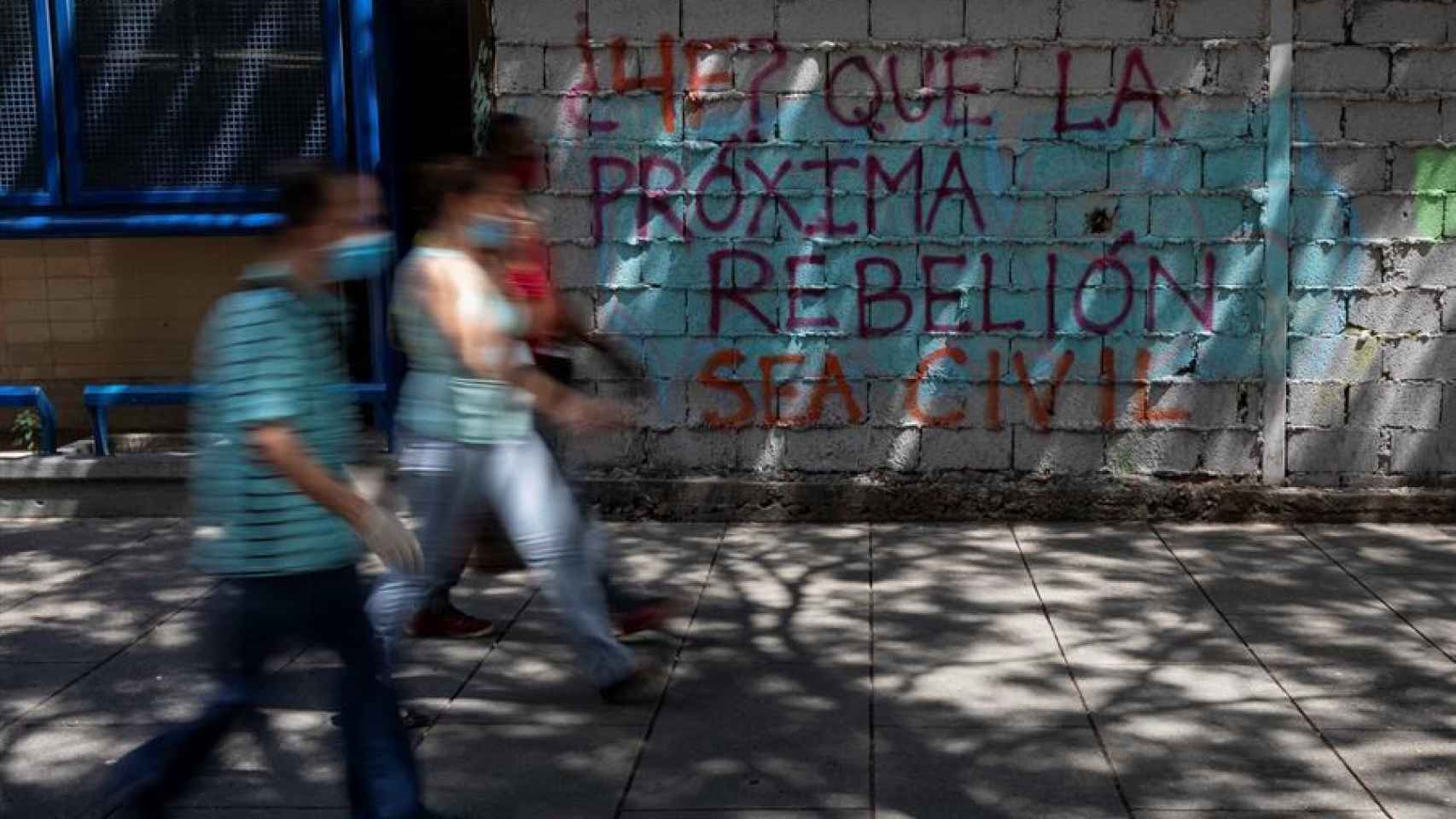 Personas caminando frente a un grafiti en Caracas.