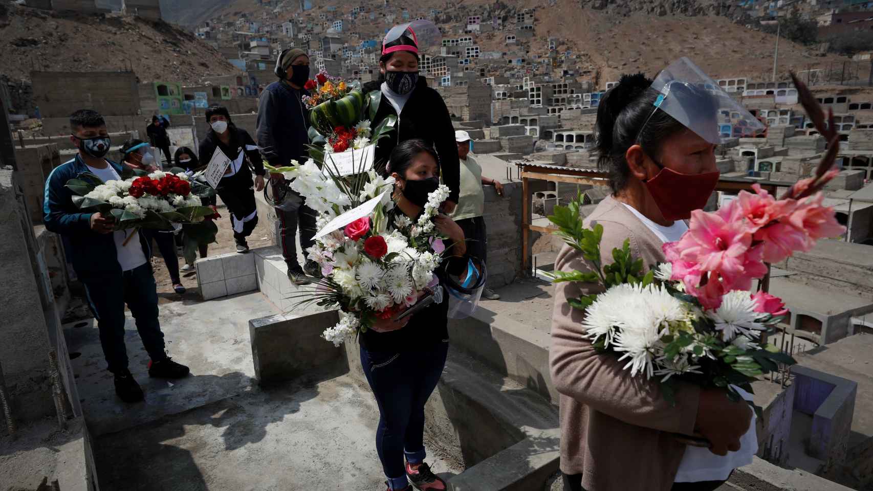 Un grupo de personas sostienen arreglos florales durante un entierro en el Cementerio del distrito de Comas.