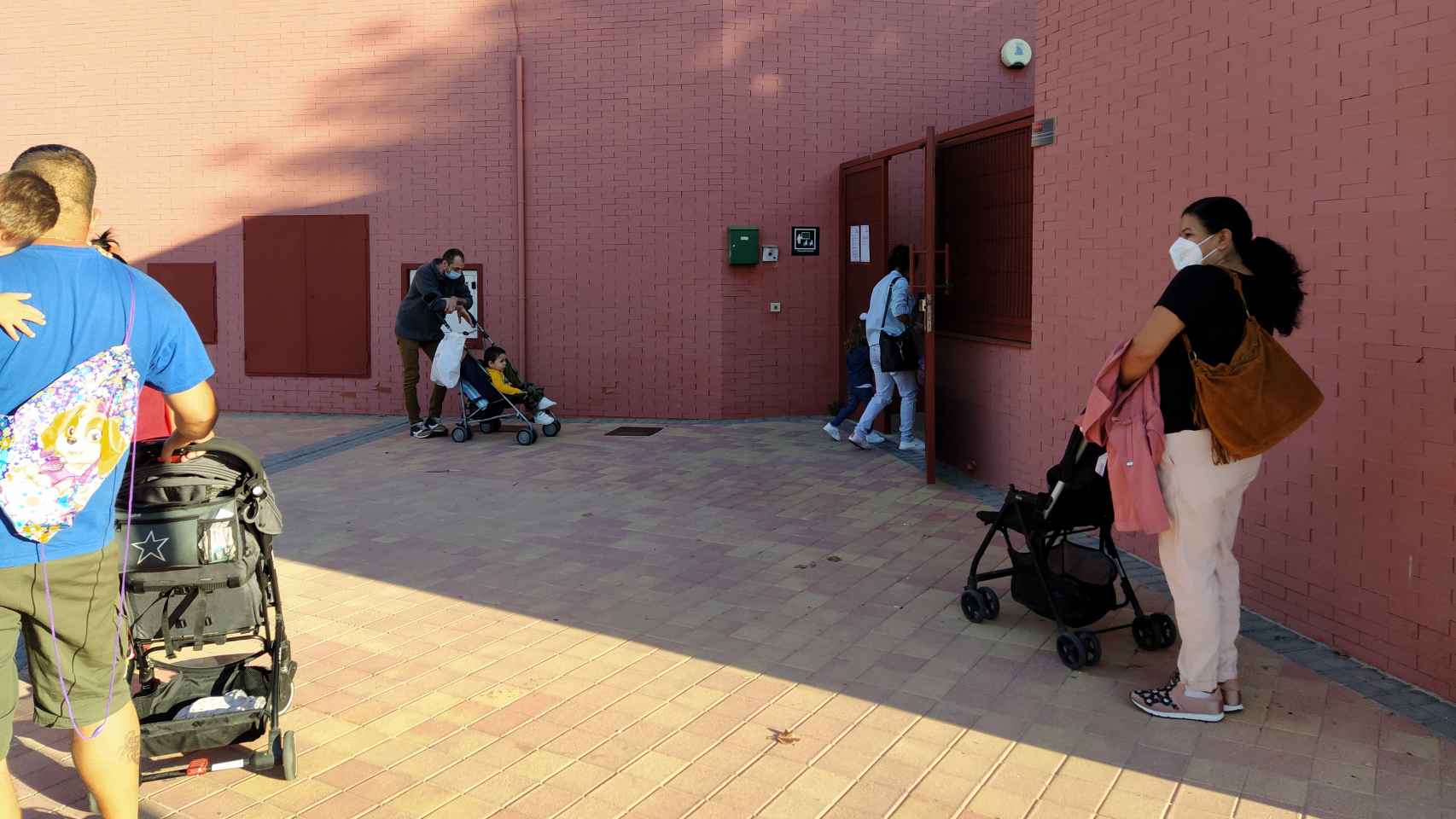 Varios padres, junto a sus hijos, esperan pacientemente a que les autoricen a acceder al centro educativo.