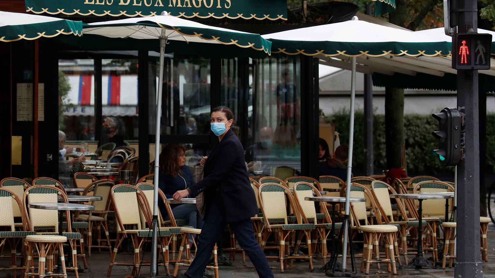 Una mujer pasea con mascarilla ante una terraza vacía de París.