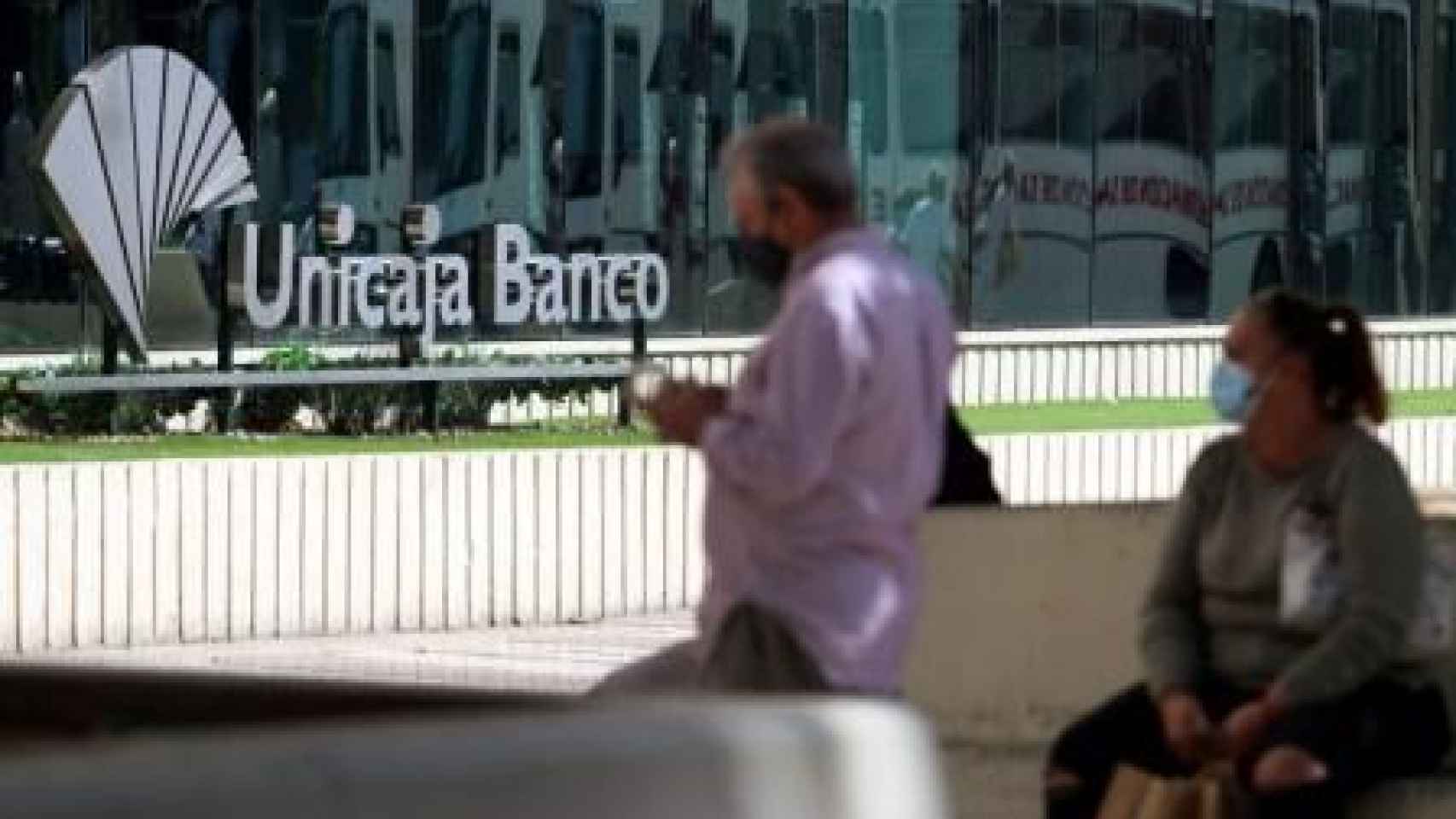 Dos personas frente a la sede de Unicaja Banco en Málaga | EP