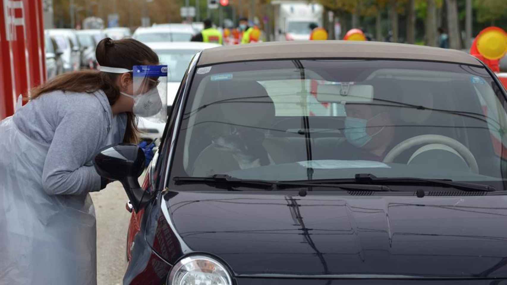 Una encargada de recoger muestras de saliva se inclina sobre el coche de uno de los usuarios.