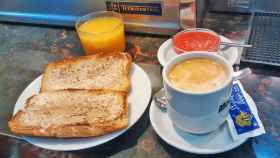 Un café con leche para desayunar con unas tostadas con tomate.