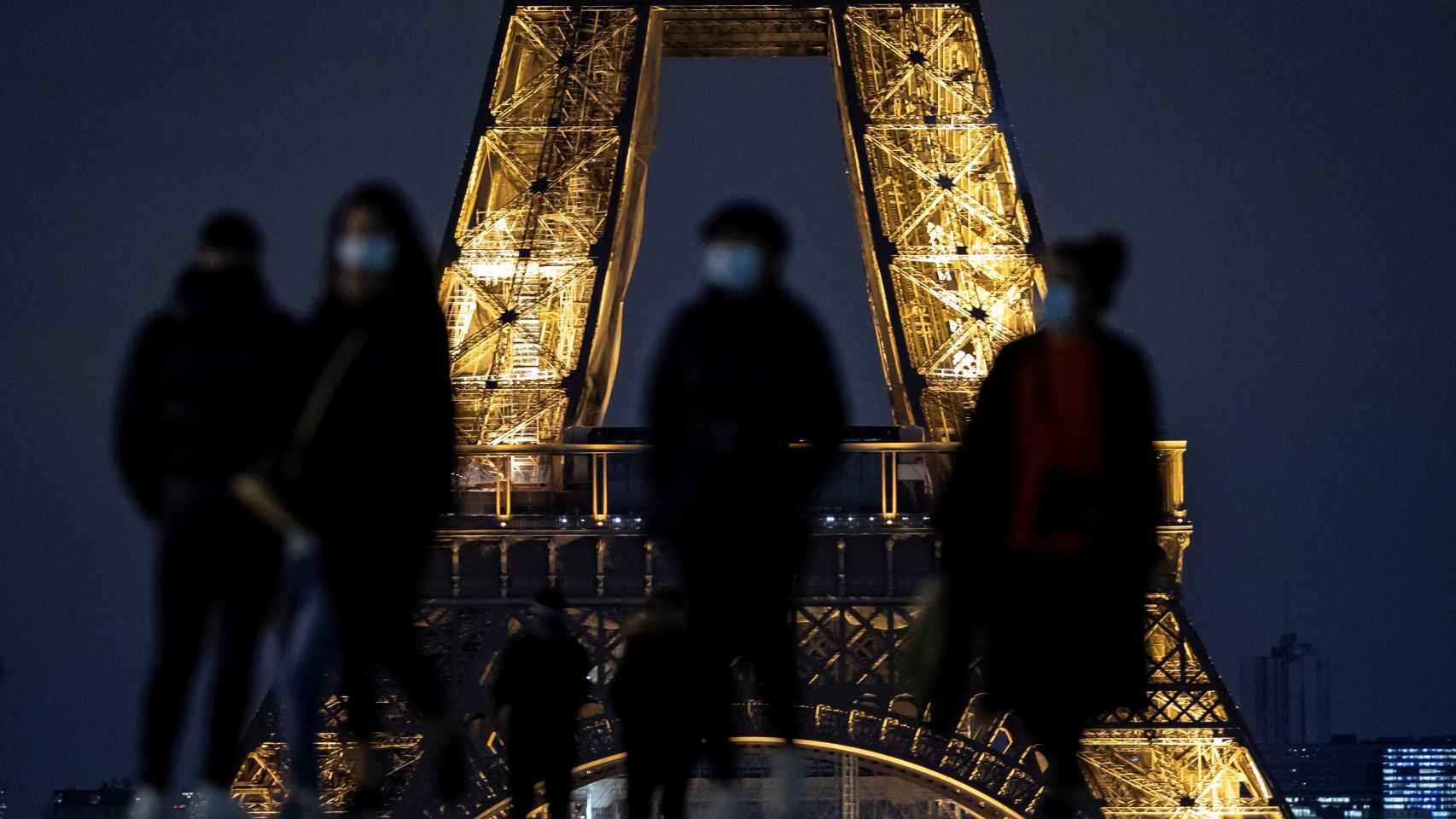 Varios transeúntes portan mascarillas ante la Torre Eiffel en París.
