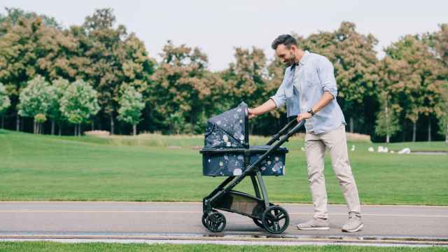 Un hombre pasea a un bebé en carrito por un parque.