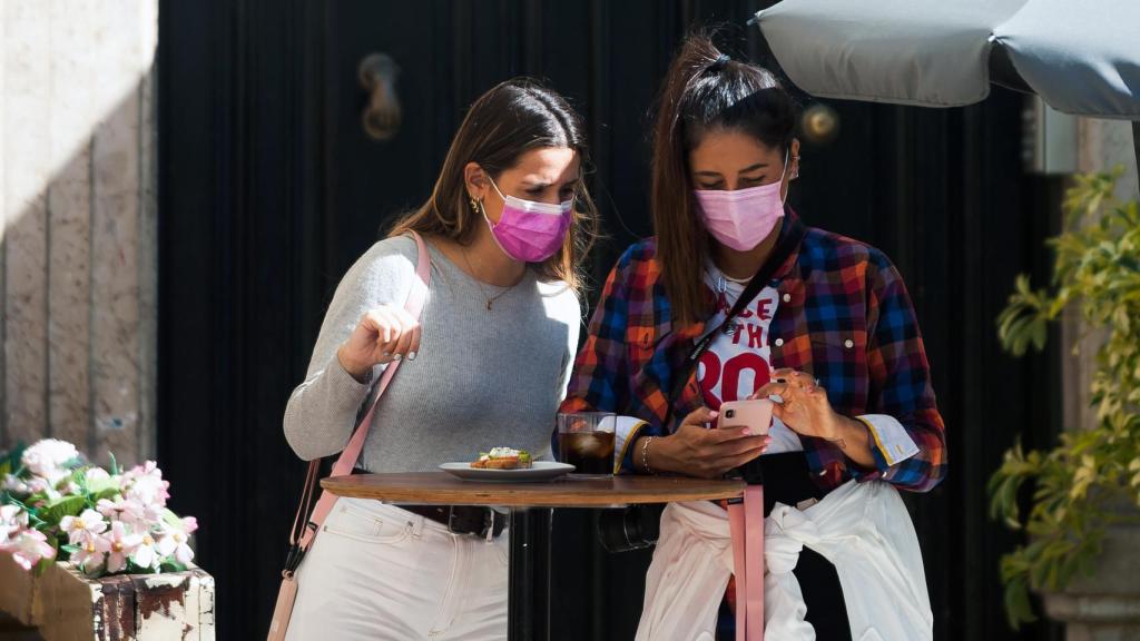 Dos jóvenes utilizando mascarillas en un bar.