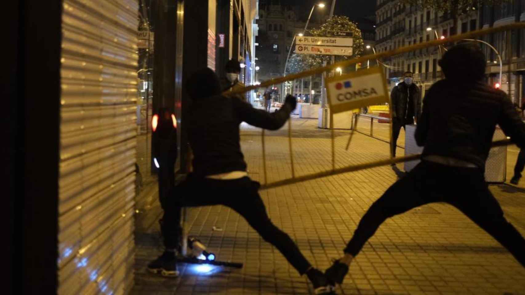 Dos hombres lanzan una valla contra un escaparate en Barcelona.