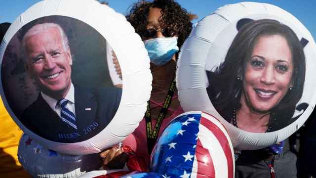 Una mujer celebrando la victoria con dos globos de Biden y Harris.